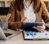 Mujer en un escritorio, mirando una tablet y descubriendo como organizar las finanzas del negocio
