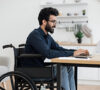 Hombre en silla de ruedas mirando los grados de discapacidad en el portátil