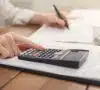 Manos de una mujer con una calculadora, descubriendo qué es el IPREM para calcularlo.