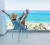 Mujer en la terraza de un piso con vistas al mar, pensando si merece la pena comprar un apartamento en la playa