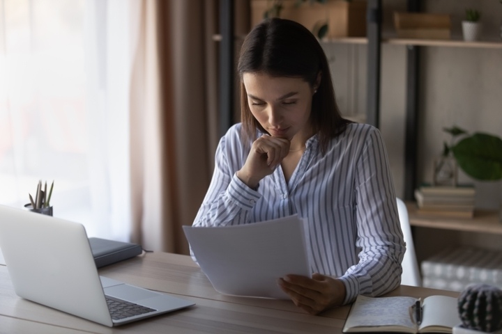 Mujer joven mirando unos papeles, revisando que debe hacer la declaración de la renta si está cobrando el paro